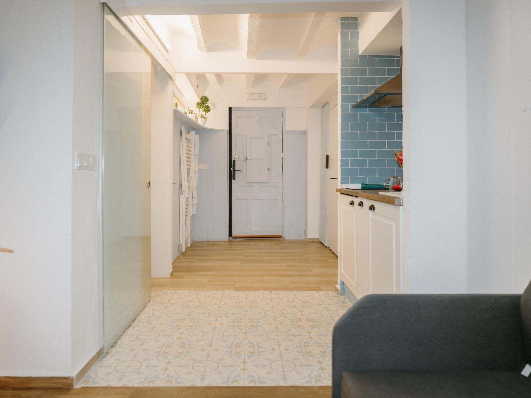 A hallway with a door at the end, a kitchen area with blue tiles, and a patterned carpet.