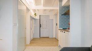 Un pasillo con una puerta al final, una zona de cocina con azulejos azules y una alfombra estampada.