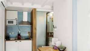 Cocina compacta con microondas, tostadora y cafetera, una mesa de madera con un tazón y copas de vino, y un salpicadero de azulejos azules.