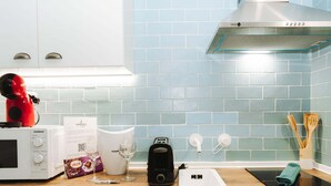 Een keuken met een magnetron, waterkoker, koffiezetapparaat, spoelbak en een houten snijplank.