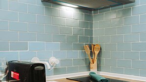 Een keuken met blauwe tegels, een broodrooster, een messenblok en houten keukengerei.