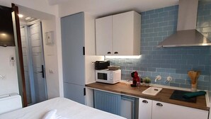 Een kleine hotelkamer met een bed, een kitchenette en een badkamer.