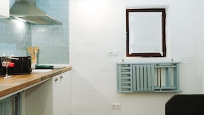 Een keuken met een magnetron, broodrooster en keukengerei op het aanrecht, een raam met een witte zonwering, en een radiator eronder.