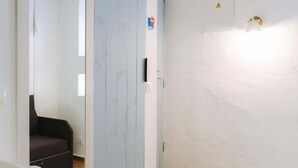 Una stanza con pavimento in legno, parete bianca, una porta e una sedia nera.