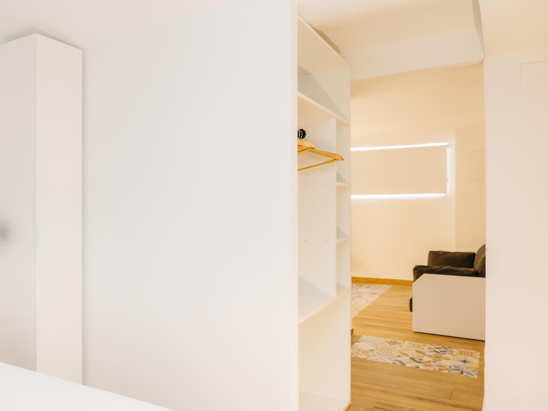 Un interior moderno con un armario blanco, suelo de madera y un sofá en una habitación luminosa.