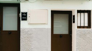 A building with three brown doors, each with a frosted glass panel. There is a sign above the left door that reads 'HARBOR'S Light MALVANIA.' - Pinot Noir Harbor's Light (La Vila Joiosa)