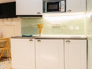 Une cuisine avec des meubles blancs, un four à micro-ondes et un dosseret de carrelage vert.