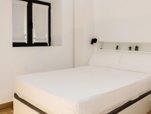 A single-bed room with a white bed, a window with black frames, and a small shelf with decorative items. - Pinot Noir Harbor's Light (La Vila Joiosa)