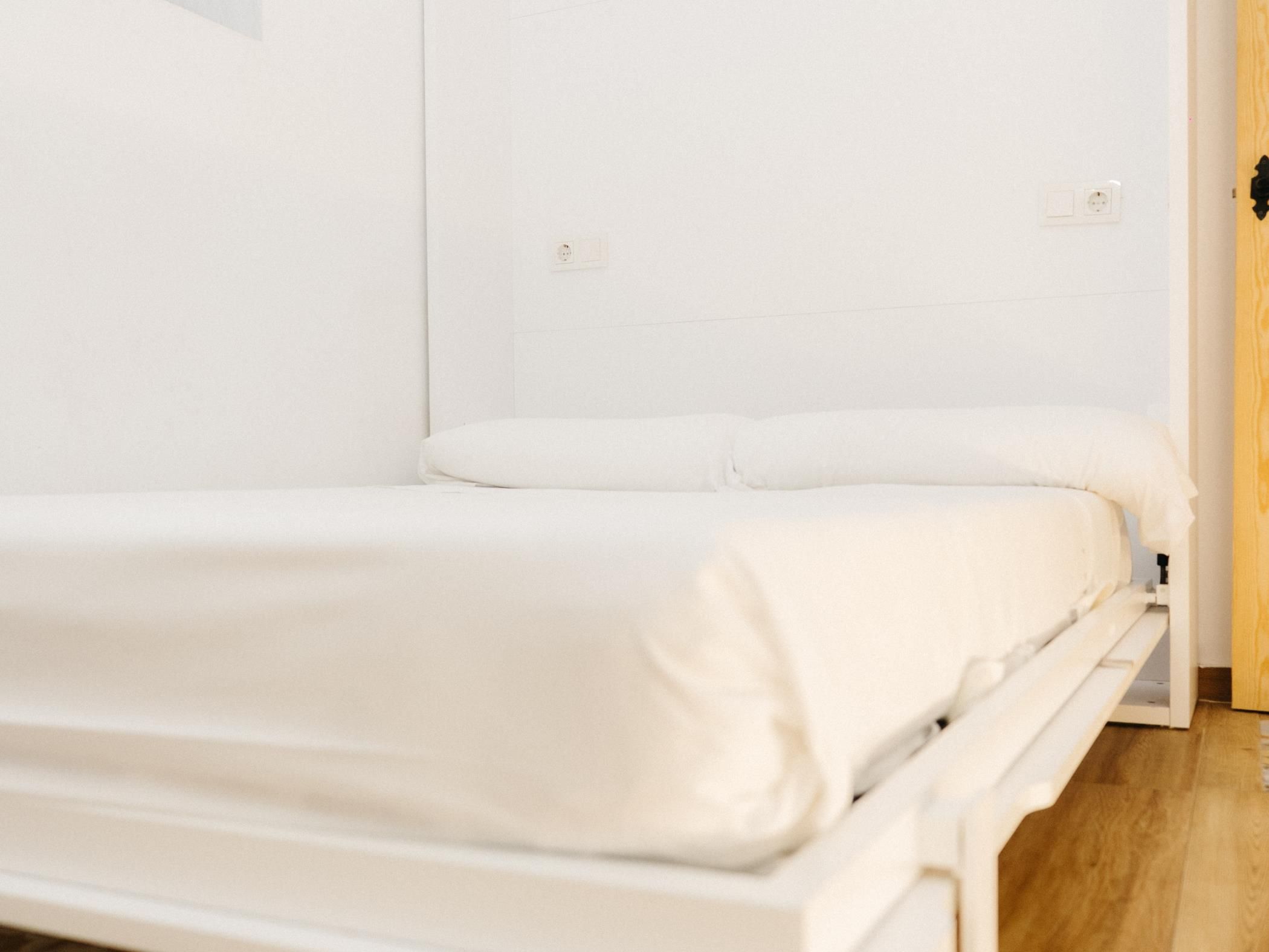A single-bed room with a wooden floor, white walls, and a white bedspread.
