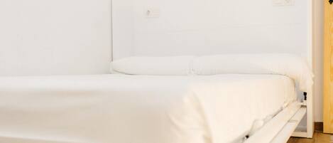 A single-bed room with a wooden floor, white walls, and a white bedspread.