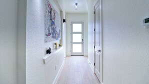 En hall med en vit dörr längst in, en taklampa och en väggmonterad termostat.