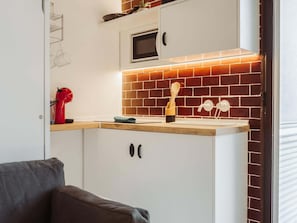 A kitchen with white cabinets, a microwave, a brick backsplash, and a wooden countertop. - Moscatel Harbor's Light (La Vila Joiosa)