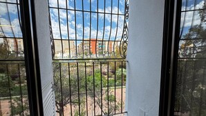 Un balcon doté d’une rambarde en métal, d’un sol carrelé et offrant une vue sur des immeubles et de la verdure.