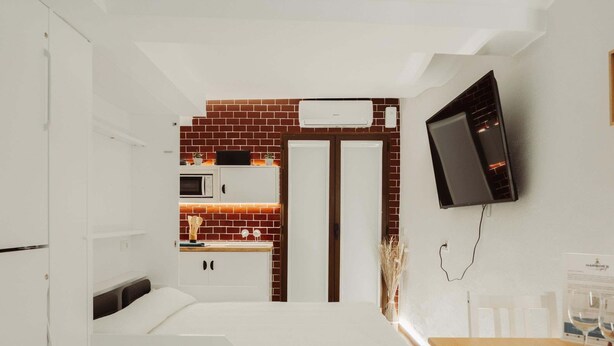 Une chambre d’hôtel compacte comprenant un lit, une petite kitchenette, une télévision et un coin repas.
