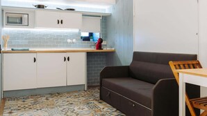 Una cocina compacta con microondas, armarios blancos, un hervidor rojo y piso estampado.