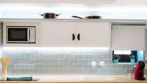 Una cocina con armarios blancos, microondas, estufa y una ventana con plantas.