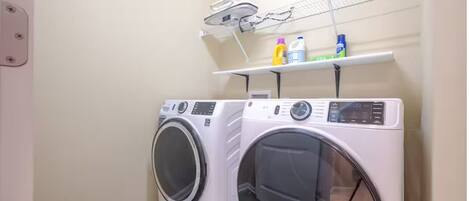 Un lavadero con dos lavadoras de carga frontal, un tendedero y una estantería con productos de limpieza.