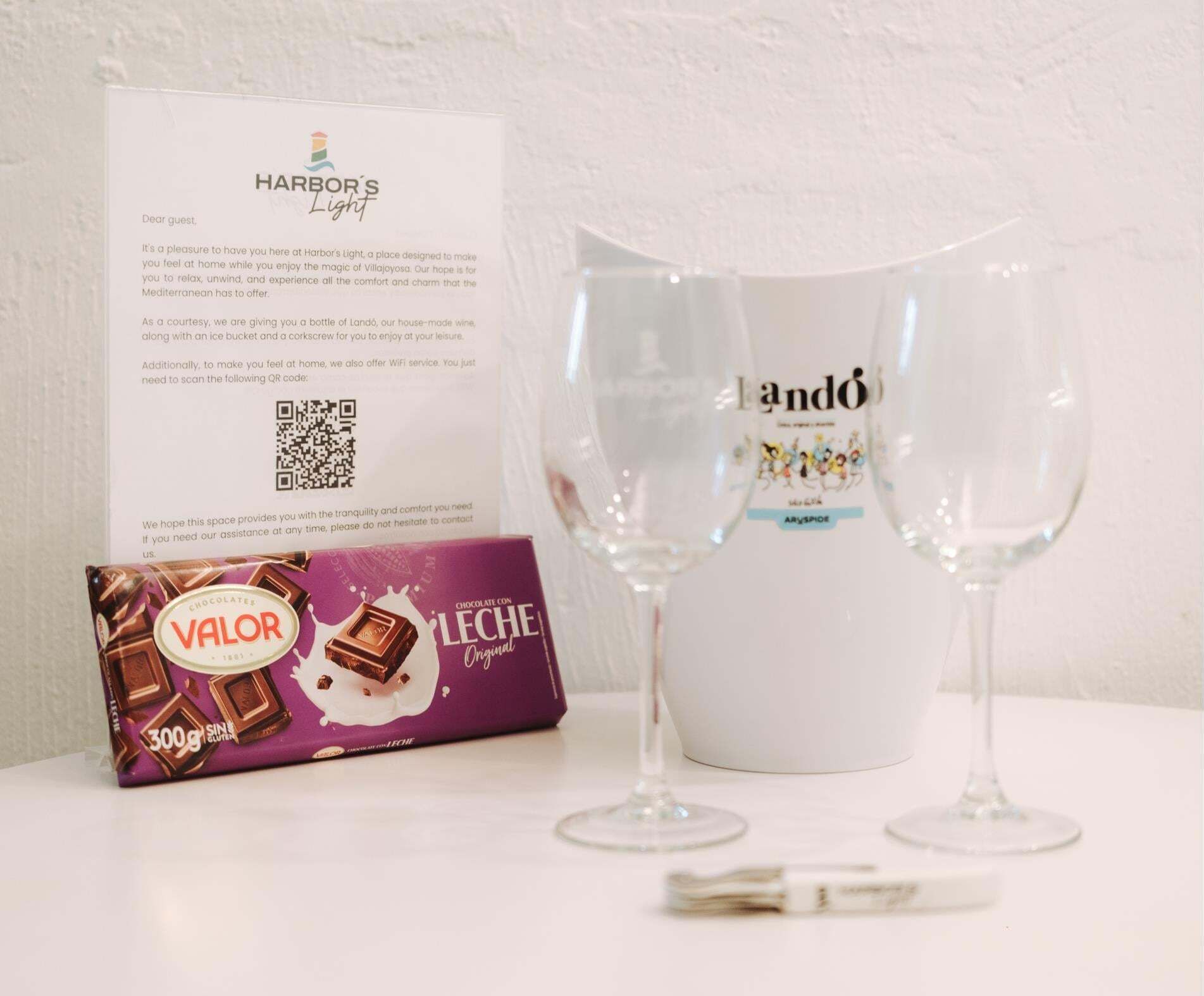A hotel sign, a bottle of Landó wine, two wine glasses, and a box of chocolates.