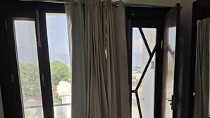 A room with a blue chair, a sliding glass door, and a view of buildings and trees. - Hotel Golden Peak (Tanakpur)