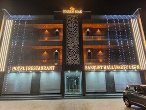 A hotel with a modern facade, featuring illuminated signs for 'Hotel Restaurant' and 'Banquet Hall Party Lawn.'