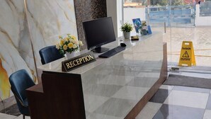 A reception desk with a marble wall, a computer, and a plant. - Hotel Golden Peak (Tanakpur)