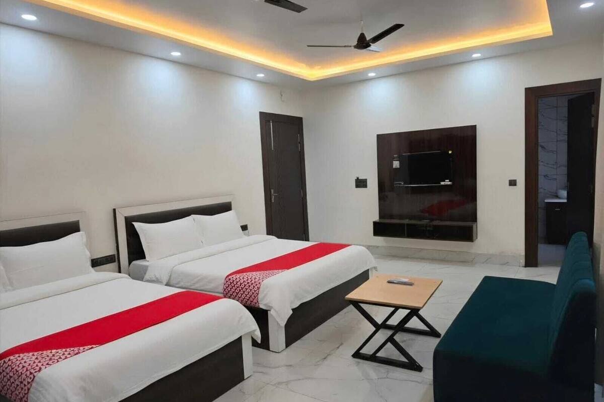 Habitación de hotel con dos camas, televisión, ventiladores de techo y una mesita.