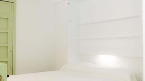Una habitación con una cama, una puerta verde y paredes blancas.