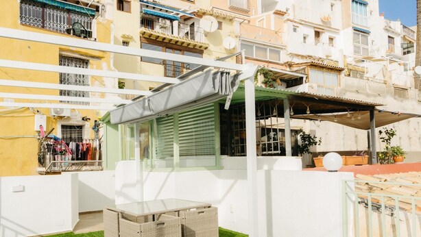 Un patio con una mesa y sillas, rodeado de edificios con balcones y antenas parabólicas.