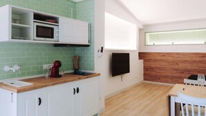 Une cuisine moderne avec des armoires blanches, un pare-feu vert, un plan de travail en bois, un four à micro-ondes, une télévision et un coin repas avec une table et des chaises.