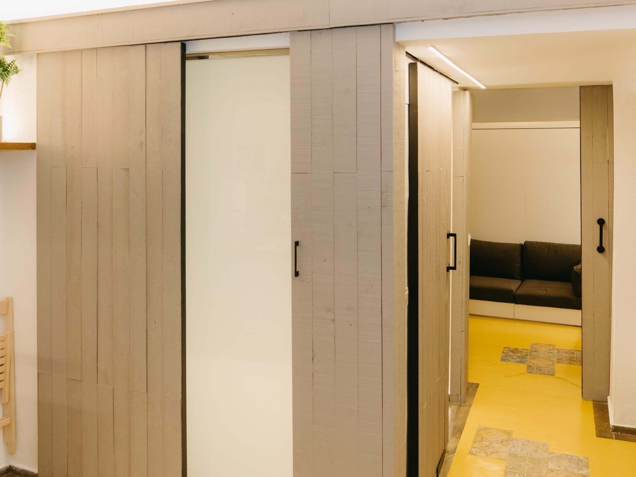 Una habitación con puerta corredera, un sofá y suelo amarillo.