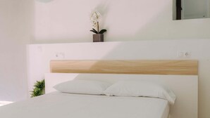 Un dormitorio con cama, mesita de noche, planta en maceta y lámpara de pared.