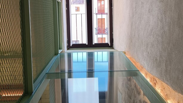 Un interior moderno con un balcón de vidrio, una pared con diseño y vistas a un edificio con balcones.