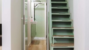 Una escalera con peldaños verdes que lleva a un baño con ducha y lavamanos.