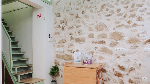 Ein Zimmer mit einer Steinsturz, einem Holztisch mit Stuhl, einer kleinen Topfpflanze und einer Treppe mit grünen Geländern.