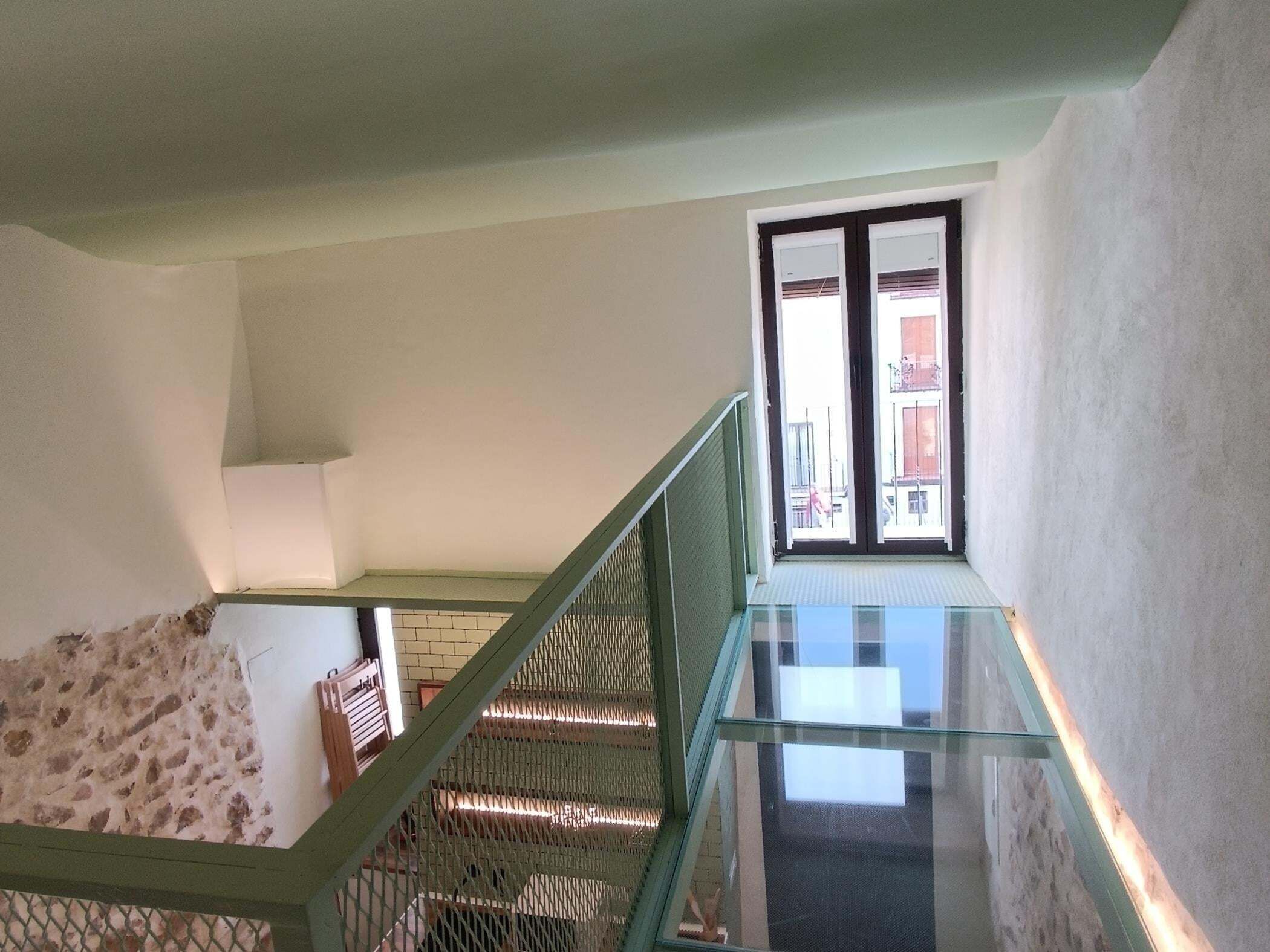 Una escalera con barandillas de vidrio que conduce a un rellano con ventanal.