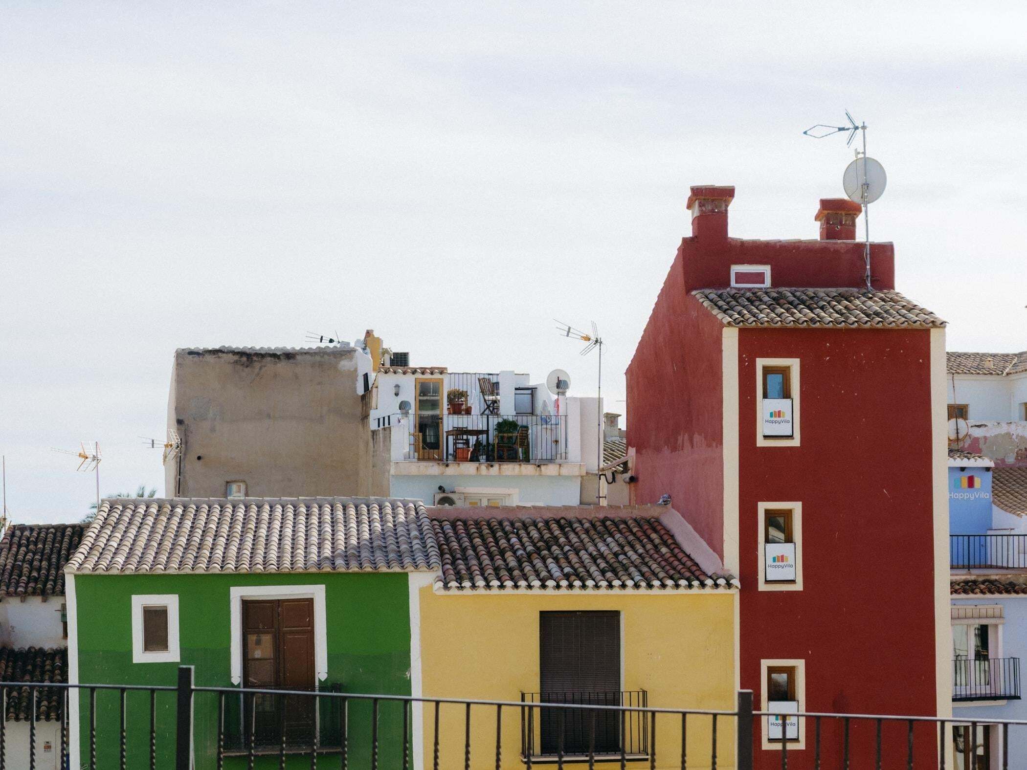 A row of colorful buildings with flat roofs, some with satellite dishes and antennas.