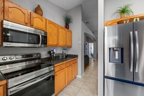 A modern kitchen with stainless steel appliances, wooden cabinets, and a tiled floor.