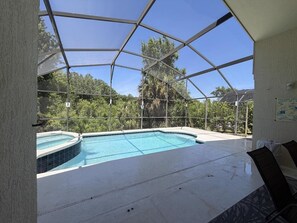 A swimming pool with a glass enclosure, surrounded by a patio area with chairs. - Aloha — A Magical Disney Retreat on Indian Creek (Kissimmee)