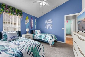 A bedroom with two beds, a ceiling fan, and a wall with surfboard decorations and a family-themed message.