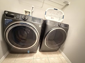 Two front-loading washing machines in a laundry room with a white door and a basket on the wall.