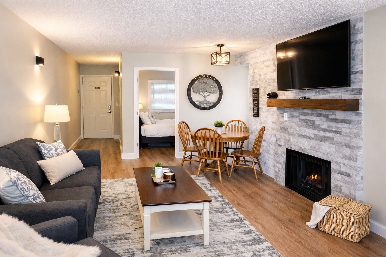 A living room with a fireplace, a TV mounted on the wall, a dining area with chairs, and a sofa with cushions.