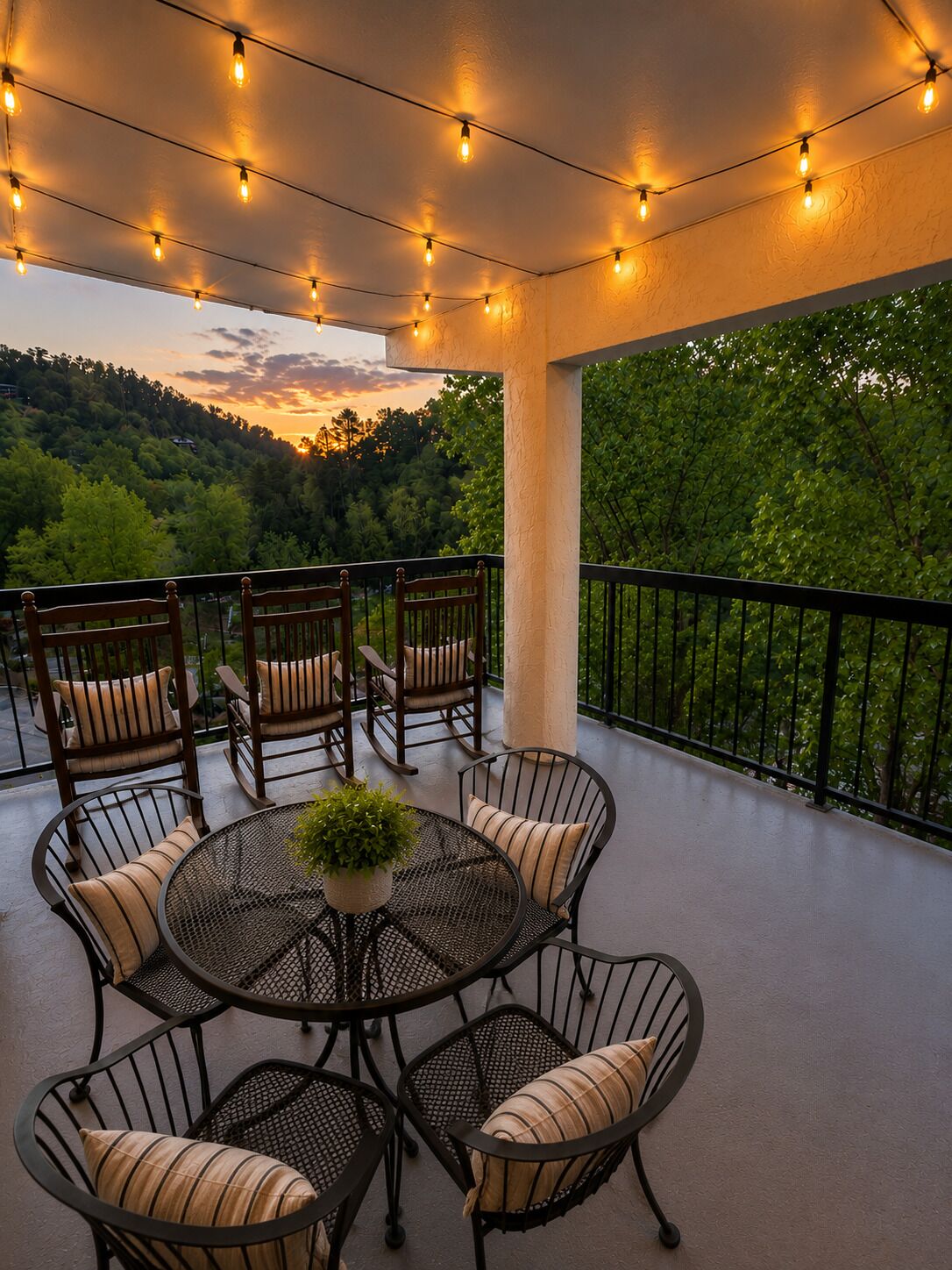 A balcony with outdoor furniture, string lights, and a view of a forested landscape.