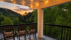 Ein Balkon mit Gartenmöbeln, Lichterketten und Blick auf eine bewaldete Landschaft.