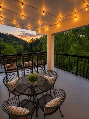 A balcony with outdoor furniture, string lights, and a view of a forested landscape. - Walk to the Strip • Mountain Views • Cozy Retreat (Gatlinburg)