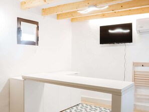 Ein Zimmer mit weißem Schreibtisch, einem an der Wand montierten Fernseher und Holzbalken an der Decke.