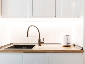 Une cuisine dotée d’un évier en acier inoxydable, d’un robinet moderne et d’une bouilloire électrique blanche posée sur le plan de travail.