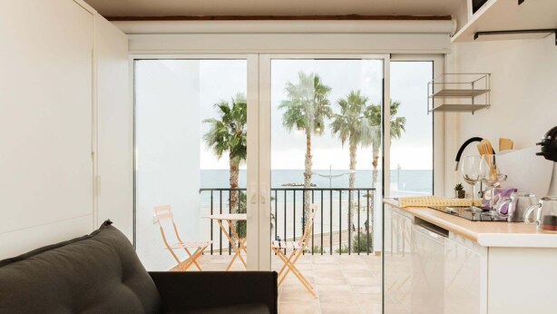 En modern inredning med en soffa, en matplats med stolar, en köksbänk och utsikt över havet med palmer.