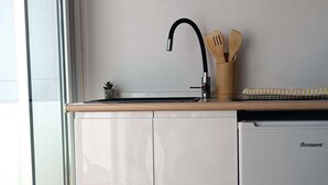 Ett kök med diskmaskin, en diskho med blandare, träredskap i ett ställ och en liten växt på bänkskivan.