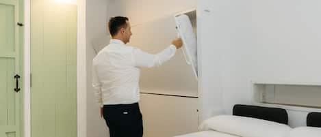 Una persona instalando un equipo blanco montado en la pared en una habitación con una cama, una puerta verde y un techo blanco.