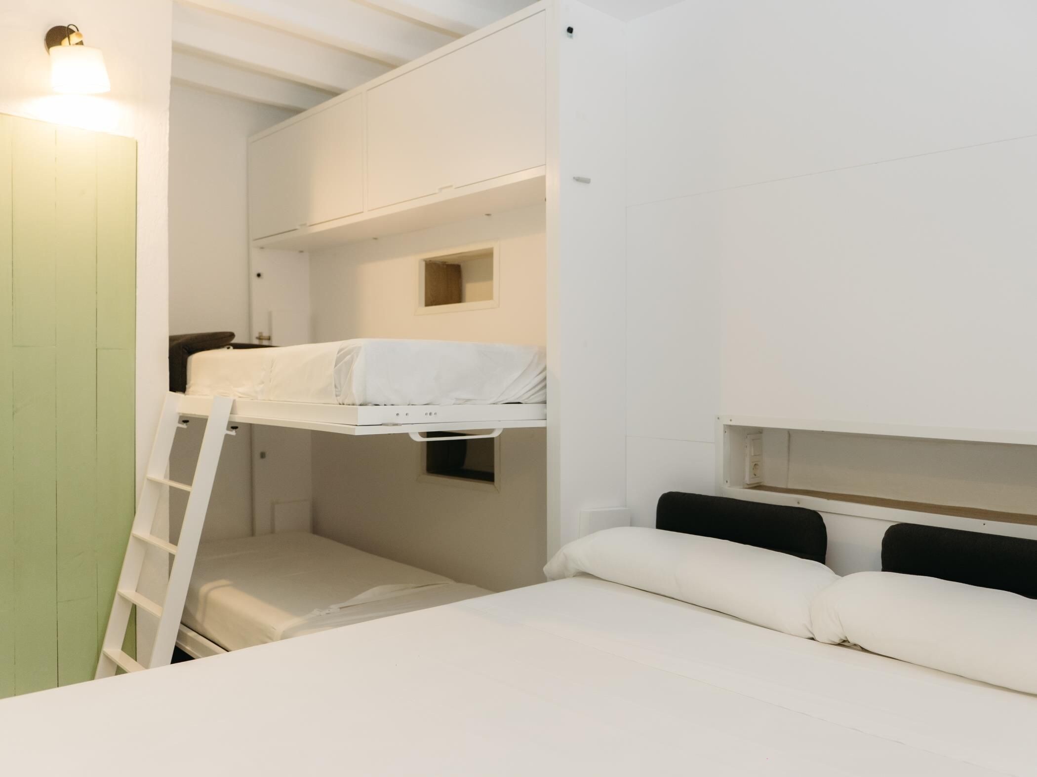 Dormitorio con literas, una escalera, una ventana pequeña y una lámpara.